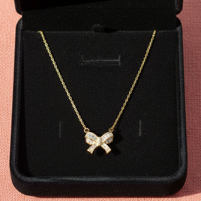 Gold necklace with a bow pendant in a black box on an orange background