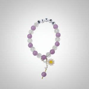 Bracelet with purple and clear beads and a flower charm on a dark surface